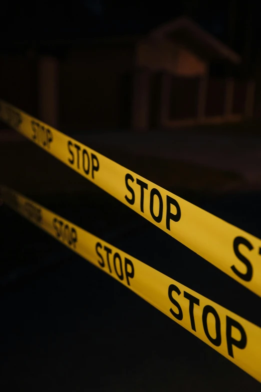 a close up of a yellow tape with a house in the background, by Carey Morris, pexels, graffiti, homicide, on black background, stop sign, cop