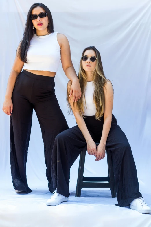 two women standing next to each other in front of a white backdrop, trending on unsplash, large pants, sitting down casually, 💣 💥💣 💥, ying and yang