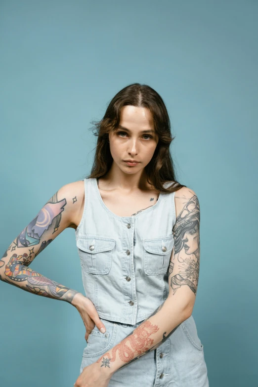 a woman with tattoos posing for a picture, inspired by Elsa Bleda, trending on pexels, hyperrealism, blue tank top, androgynous person, solid background, grey backdrop