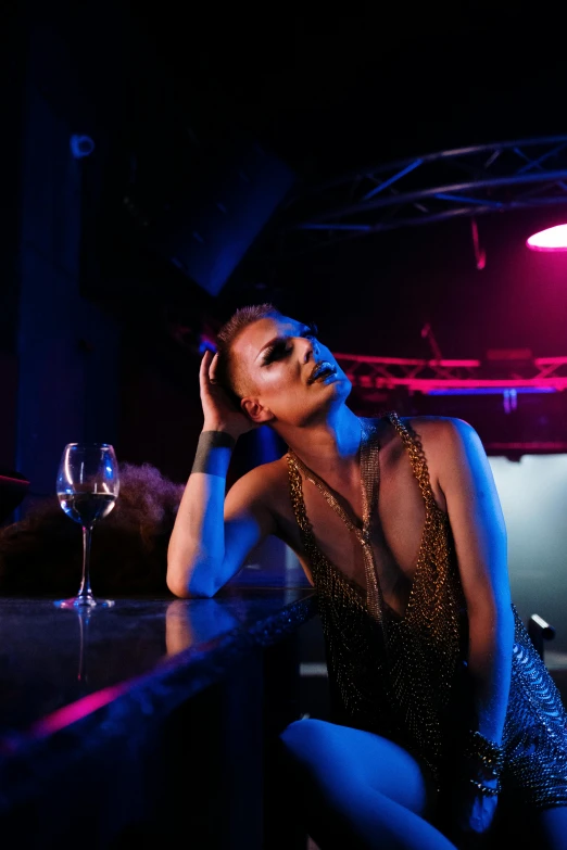 a woman sitting on top of a bar next to a glass of wine, inspired by Nan Goldin, trending on pexels, renaissance, drag queen, stage at a club, looking sad, dancefloor kismet