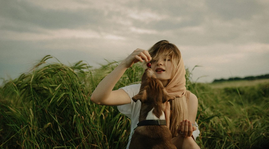 a woman standing in a field of tall grass, trending on pexels, holding a boxer puppy, wearing a head scarf, gemma chan beautiful girl, having a snack