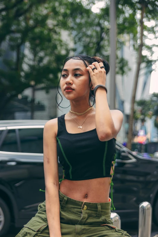 a woman sitting on a fire hydrant talking on a cell phone, an album cover, inspired by Ruth Jên, trending on pexels, wearing a cropped black tank top, black and green, indonesia, standing in a city street