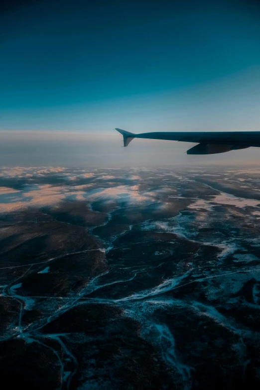 an airplane wing flying over a body of water, pexels contest winner, precisionism, desolate arctic landscape, flowing curves, minn, yeg