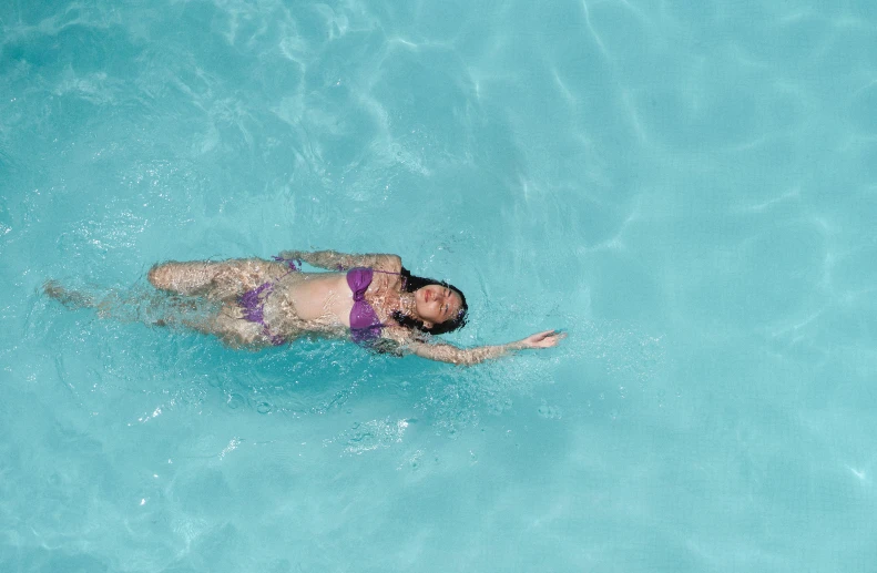 a woman in a bikini swims in a pool, by Carey Morris, pexels contest winner, purple, aquamarine, full lenght, top-down shot