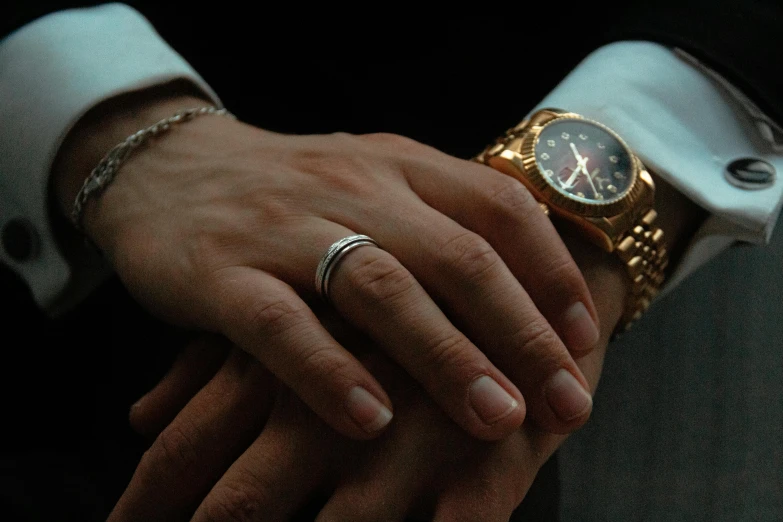 a close up of a person holding a wrist with a watch on it, an album cover, inspired by L. A. Ring, an elegant couple, profile image, reddit post, wearing two metallic rings