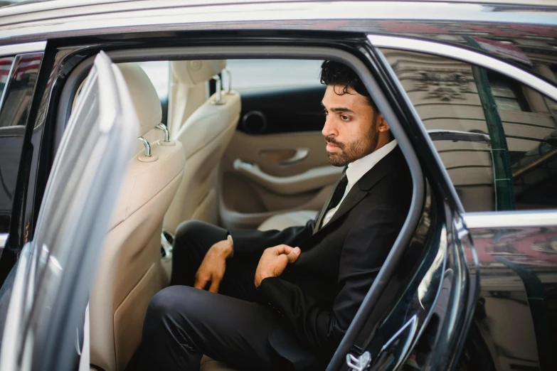 a man sitting in the passenger seat of a car, pexels contest winner, hurufiyya, wearing a black suit, avatar image, formal wear, half turned around