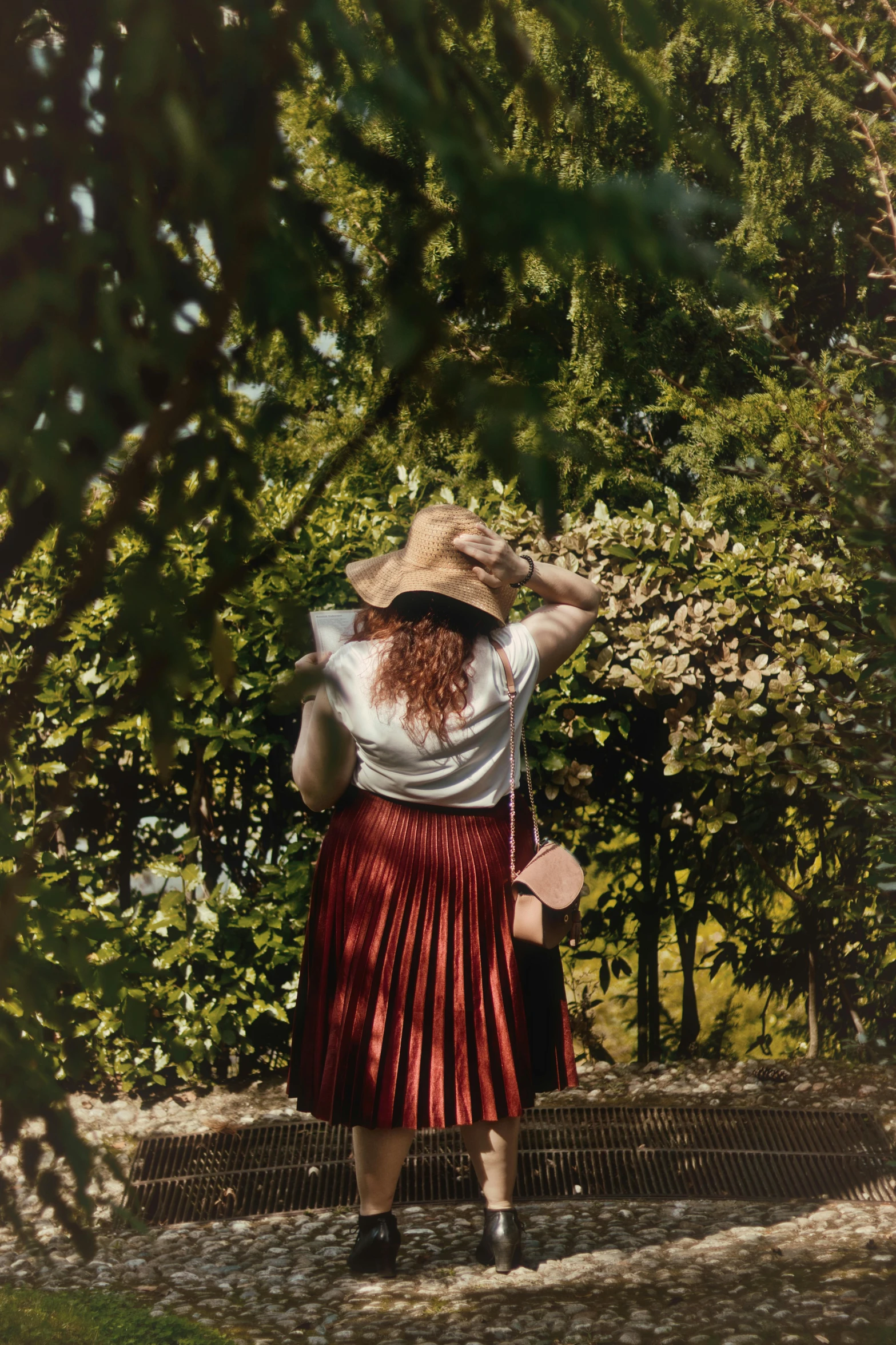 a woman walking down a path with a hat on, inspired by Louis Stettner, pexels contest winner, renaissance, with a red skirt, ( redhead, against the backdrop of trees, pleated skirt