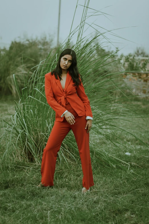 a woman in a red suit standing in the grass, an album cover, pexels contest winner, dressed in a jodhpuri suit, cindy avelino, wearing an orange jumpsuit, wearing a pinstripe suit