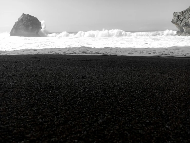 a black sand beach with two large rocks sticking out of the water, a black and white photo, by Lucia Peka, black!!!!! background, ocean floor, zoomed in shots, monster ashore