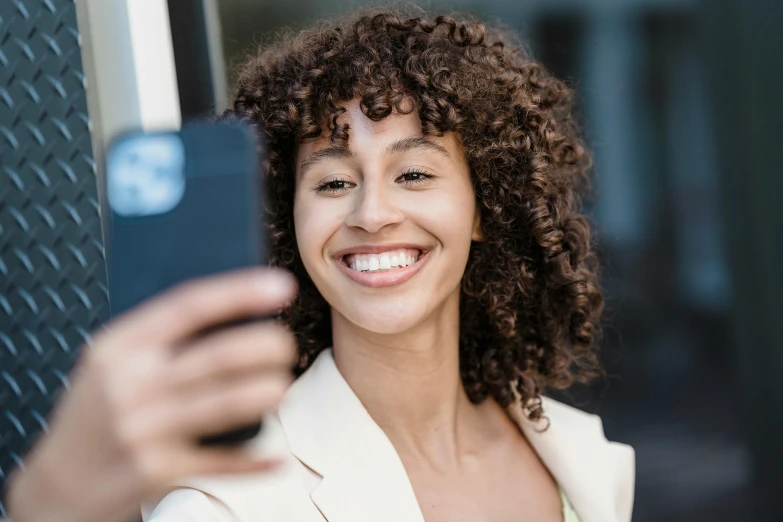 a woman taking a selfie with her cell phone, trending on pexels, brown curly hair, professional headshot, rounded corners, digital image