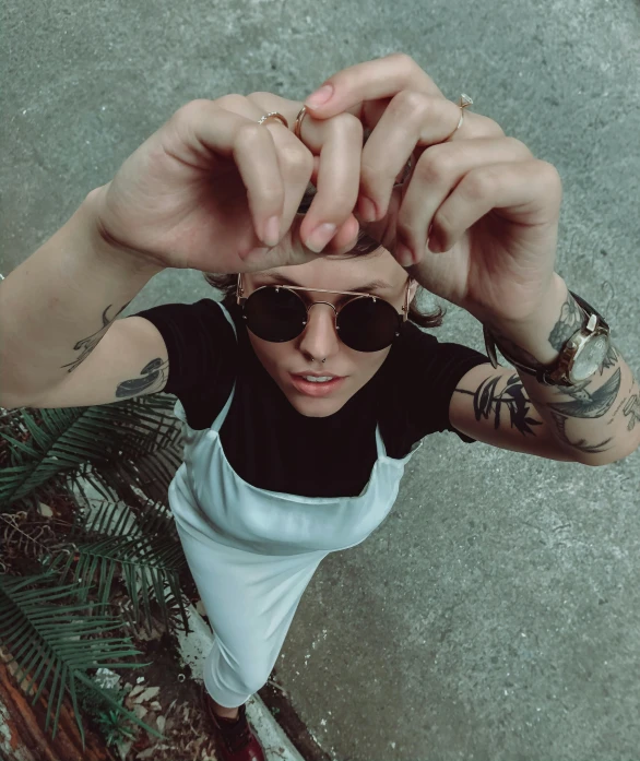 a close up of a person with tattoos on their arms, inspired by Elsa Bleda, trending on pexels, circular sunglasses, looking up at camera, tomboy, high angle shot