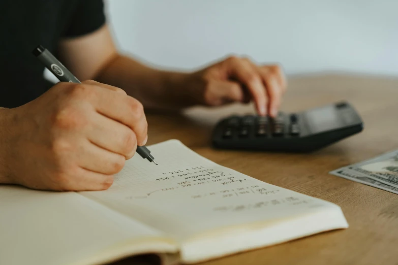 a person sitting at a table with a calculator and a pen, by Sam Charles, pexels contest winner, found scribbled in a notebook, thumbnail, plain background, te pae