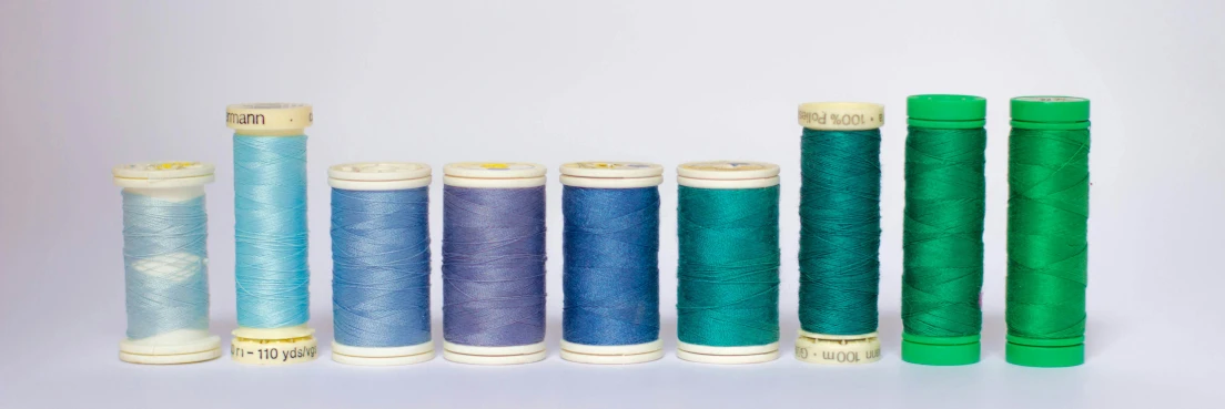a row of spools of thread sitting next to each other, by Sylvia Wishart, unsplash, arts and crafts movement, blue and purple and green, set against a white background, vintage colours 1 9 5 0 s, wearing blue