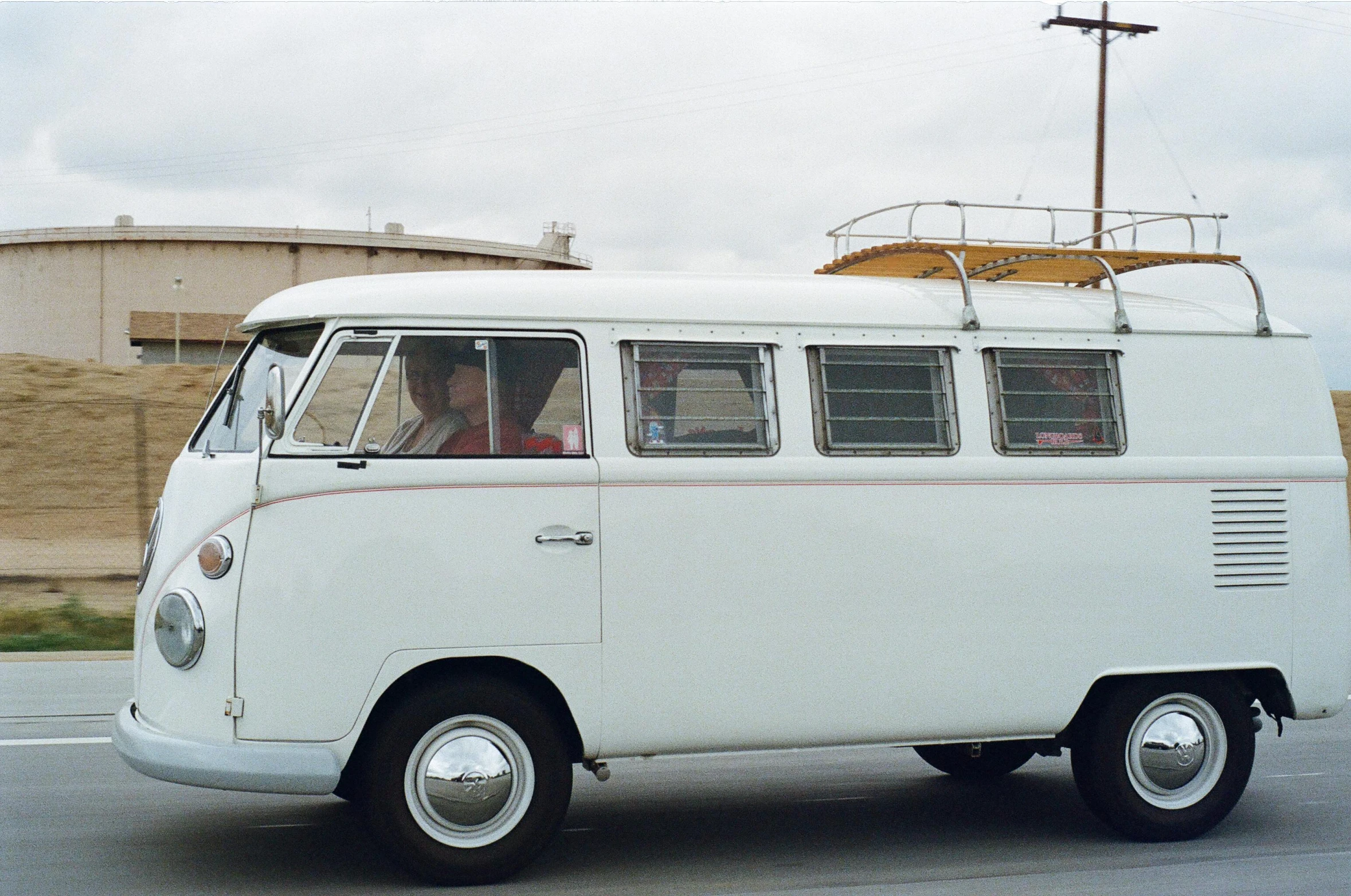 a white van driving down a street next to a building, a colorized photo, by Lee Loughridge, unsplash, vw microbus driving, cars and people, adrian tomine, southern california