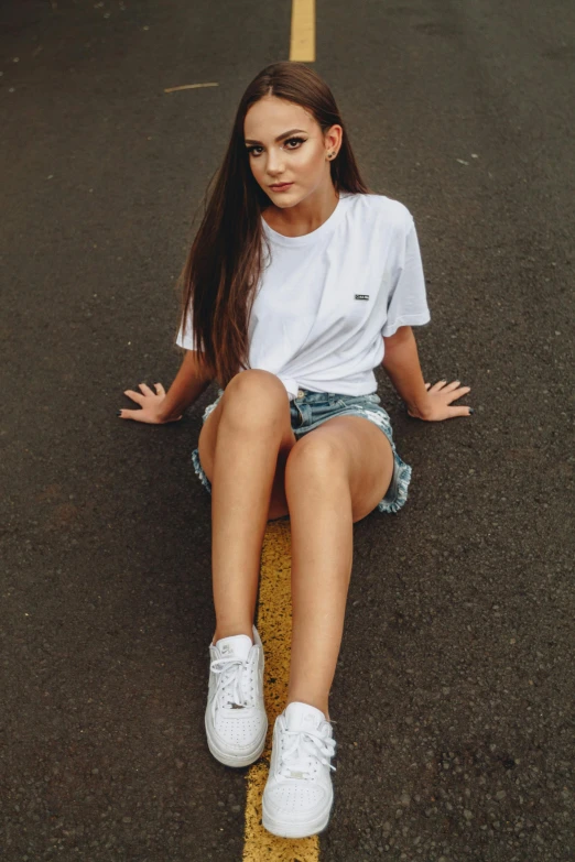 a young woman sitting on the side of a road, by John Luke, pexels contest winner, tan skin a tee shirt and shorts, white backround, white shoes, pretty oval face