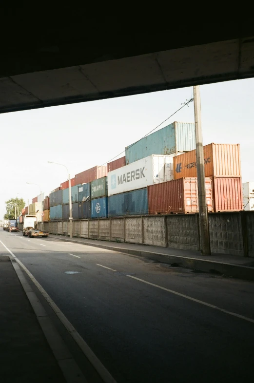 a man riding a skateboard down the side of a road, shipping containers, under bridge, jerez, stacks