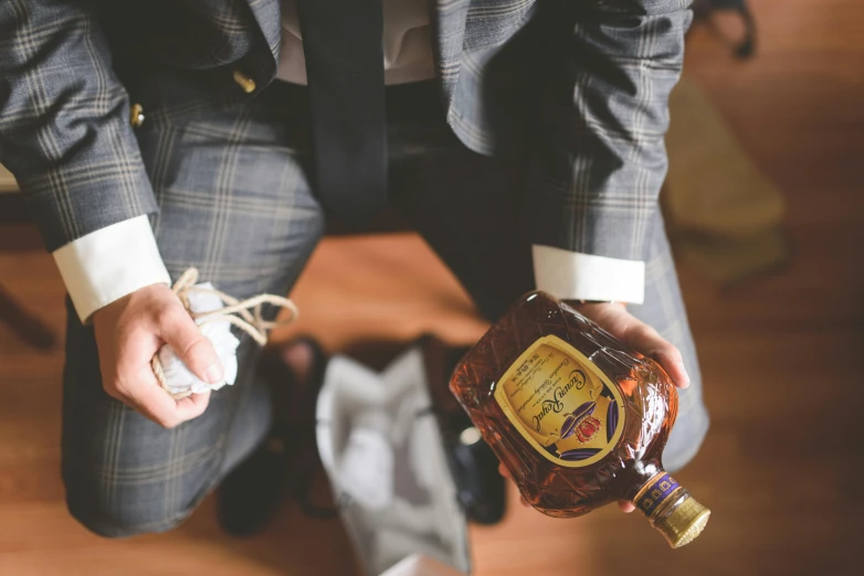a man in a suit holding a bottle of liquor, by Julia Pishtar, pexels contest winner, renaissance, sitting on the floor, holding a gold bag, windsor knot tie, caramel. rugged