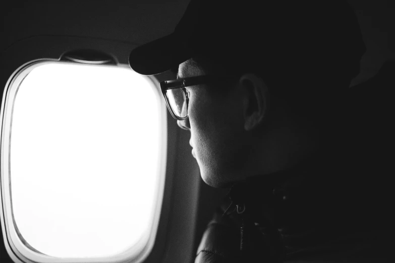 a black and white photo of a man looking out an airplane window, visual art, wearing square glasses, jesper esjing, profile image, high quality upload