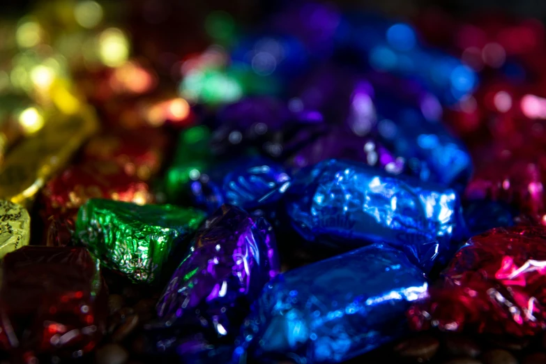 a pile of foil wrapped candy sitting on top of a table, a macro photograph, by Julia Pishtar, colour led, indigo rainbow, chocolate, roygbiv