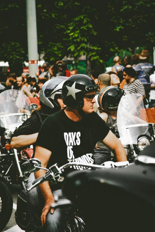 a group of people riding motorcycles down a street, he is wearing a black t-shirt, glory days, wearing ornate helmet, 🚿🗝📝