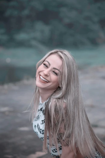 a woman standing on top of a beach next to a body of water, a colorized photo, inspired by Elsa Bleda, pexels contest winner, big smile white teeth, tags: blonde hair, in sao paulo, headshot profile picture