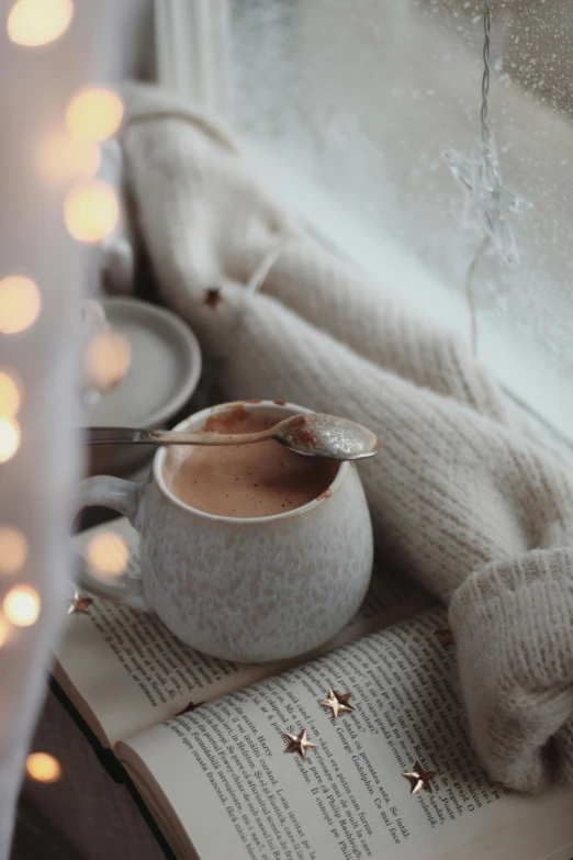 a cup of coffee sitting on top of an open book, by Elaine Hamilton, trending on pexels, romanticism, fairy lights, cream and white color scheme, gif, soup