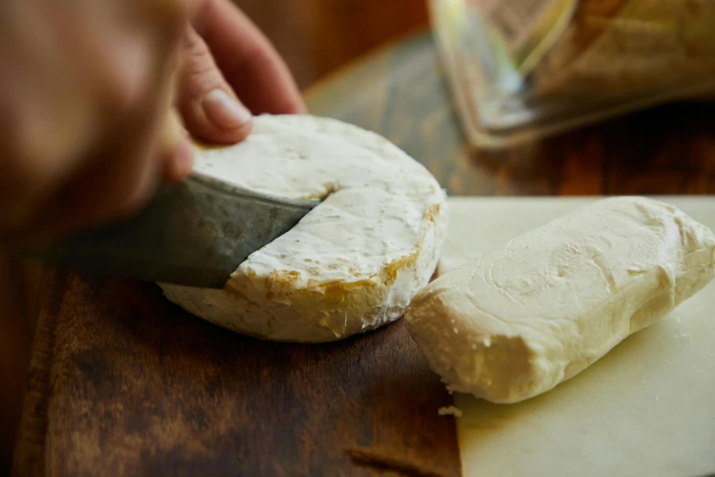 a person cutting a piece of cheese on a cutting board, by Tom Bonson, round-cropped, cream, foil, thumbnail