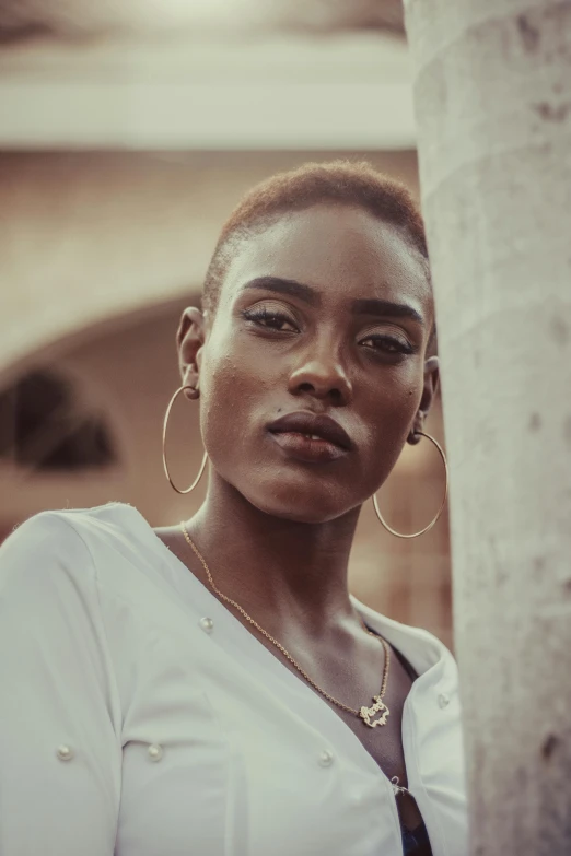 a woman in a white shirt standing next to a tree, inspired by Theo Constanté, trending on unsplash, brown skin. light makeup, cuban women in havana, non binary model, giant earrings