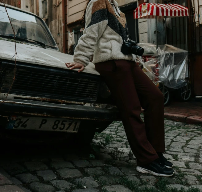a woman sitting on the hood of a car, pexels contest winner, brown pants, sovietwave aesthetic, maroon and white, clothed in ancient street wear