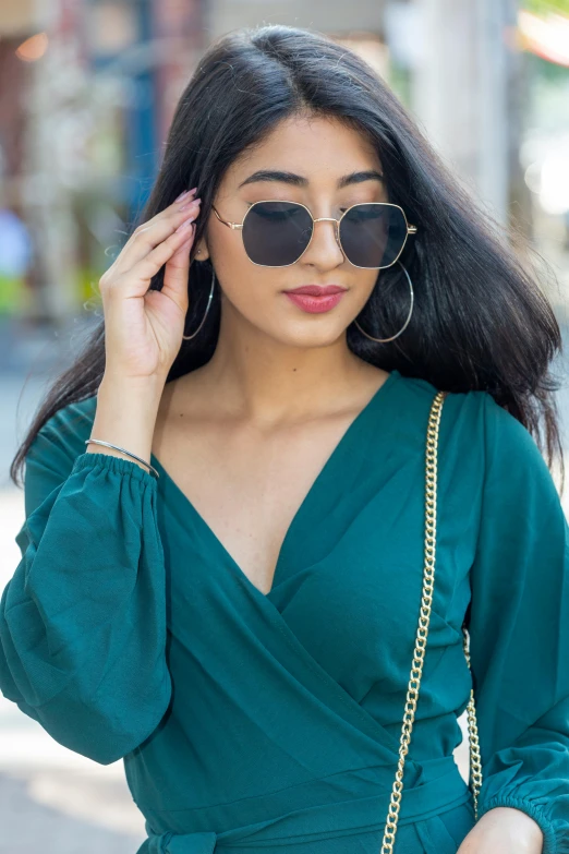 a woman in a green dress is walking down the street, inspired by Ruth Jên, trending on pexels, square glasses, beautiful asian girl, middle eastern, gold