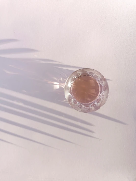 a glass of water sitting on top of a table, by Rebecca Horn, trending on unsplash, light and space, brown and pink color scheme, photograph from above, ring light, sun puddle