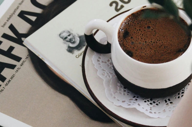 a cup of coffee sitting on top of a book, on a table, brown and white color scheme, kafka, promo image