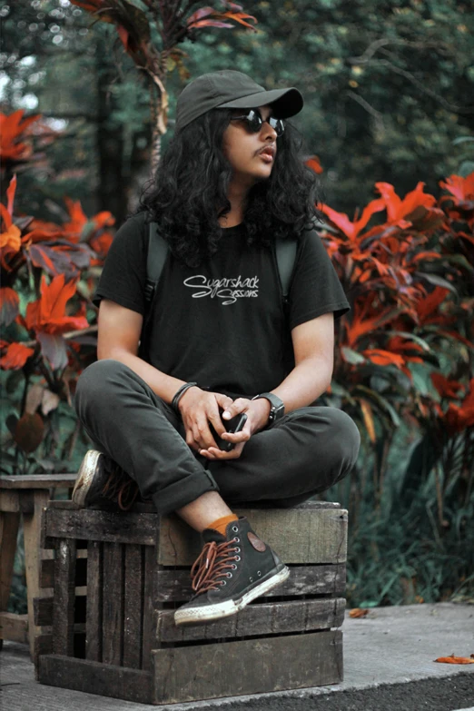 a man sitting on top of a wooden box, inspired by Rudy Siswanto, pexels contest winner, sumatraism, long wild black curly hair, black t shirt, foliage clothing, sneaker photo