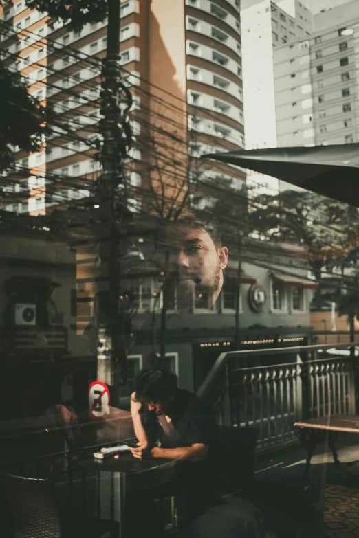 a man sitting at a table in front of a window, a picture, pexels contest winner, city reflection, cafe, in sao paulo, gif