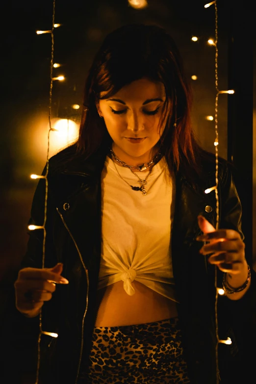 a woman looking at her cell phone in the dark, a portrait, inspired by Elsa Bleda, trending on pexels, dressed in short leather jacket, string lights, full frontal lighting, morning lighting