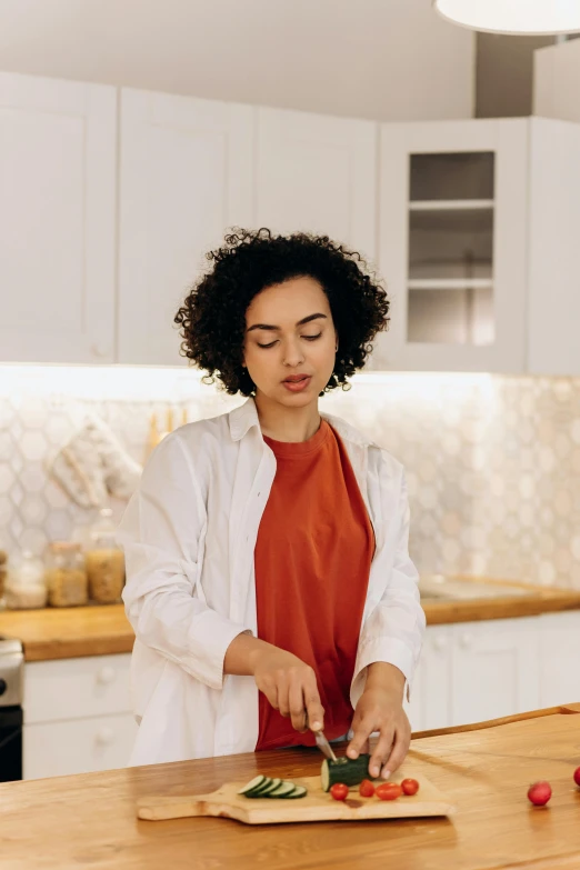 a woman cutting vegetables on a cutting board in a kitchen, pexels contest winner, lab coat and tee shirt, curly haired, architect, gif