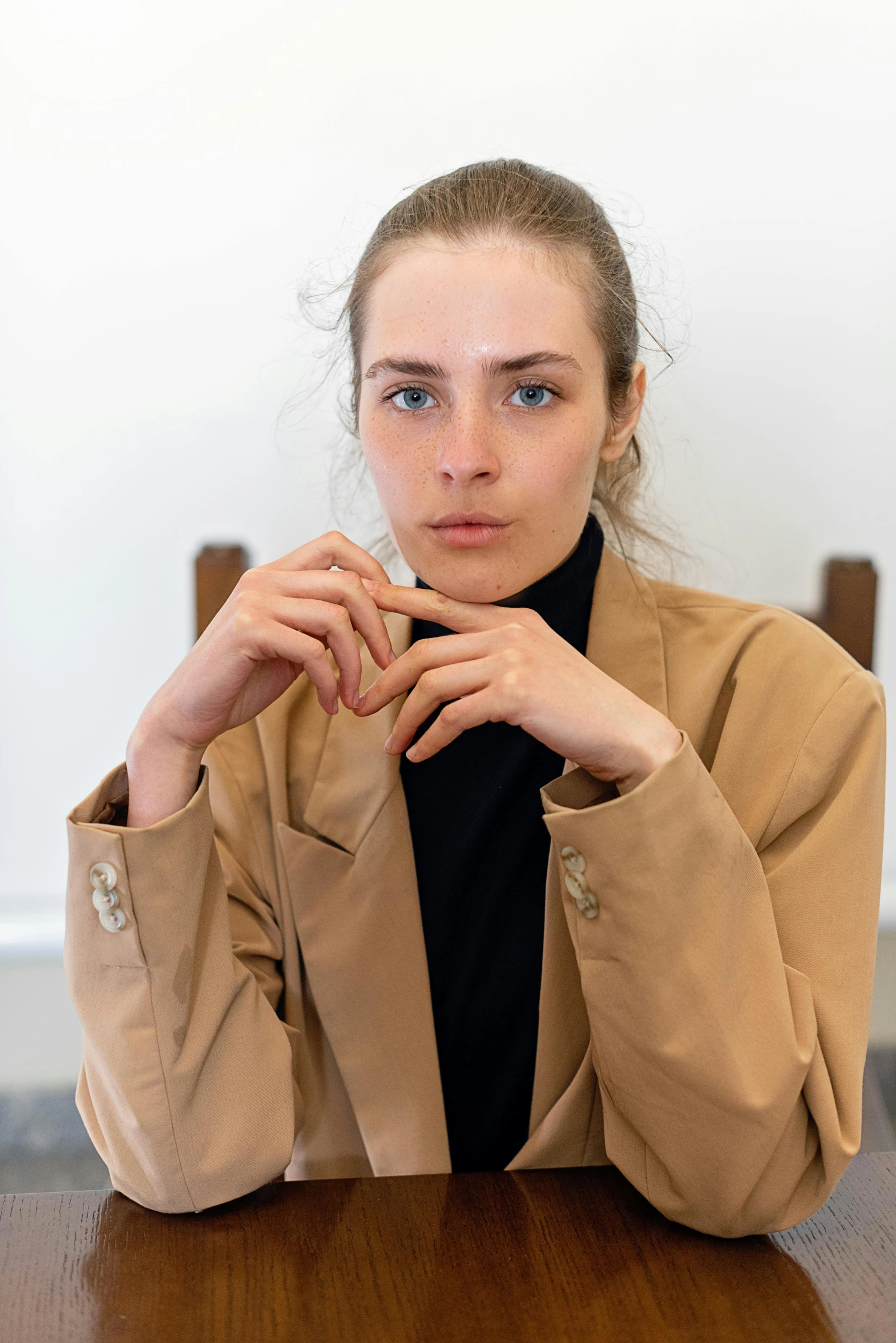 a woman sitting at a table making a heart with her hands, a character portrait, by Nina Hamnett, trending on unsplash, visual art, light brown trenchcoat, fashionweek backstage, looking serious, well-groomed model