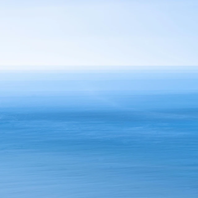 a man riding a surfboard on top of a sandy beach, a minimalist painting, inspired by Andreas Gursky, unsplash, minimalism, lots blue colours, long exposure photograph, blue submarine no 6, looking out over the sea