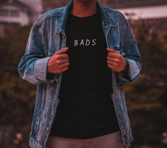 a man wearing a t - shirt that says bads, inspired by Bascove, trending on unsplash, wearing a jeans jackets, dystopian bad vibes, dark university aesthetic, product introduction photo