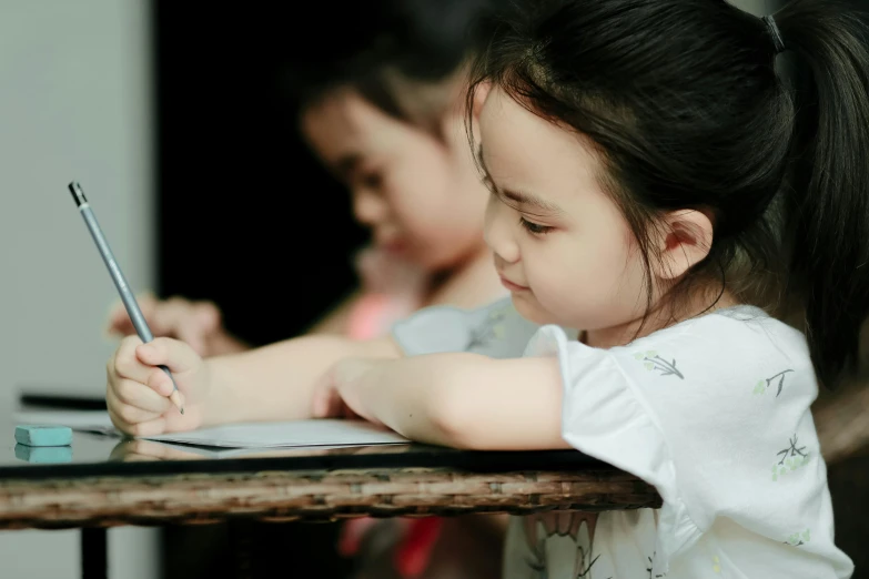 a little girl sitting at a table writing on a piece of paper, pexels contest winner, two girls, phong shaded, youtube thumbnail, background image