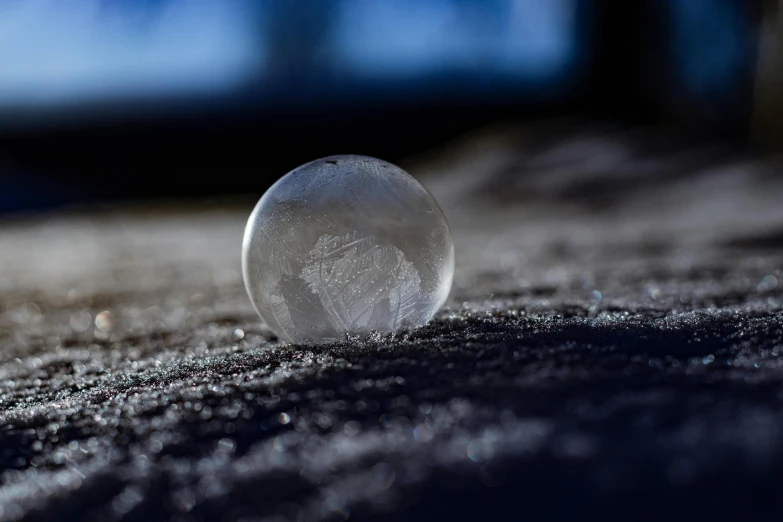 a glass ball sitting on top of a snow covered ground, a macro photograph, pexels contest winner, on the concrete ground, moonstone, flattened, semi-transparent