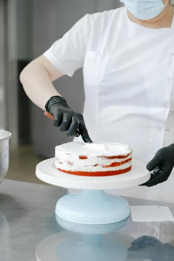 a woman in a face mask is decorating a cake, by Dan Content, pexels, white and red color scheme, silicone skin, tall, piping