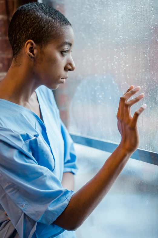 a woman looking out a window on a rainy day, wearing a hospital gown, comforting, photo of a black woman, cracked windows