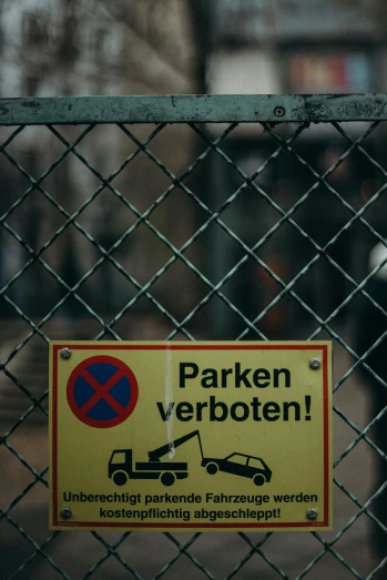 a no parking sign on a chain link fence, a poster, by Sebastian Spreng, pexels, wrecked cars, square, german, low quality photo