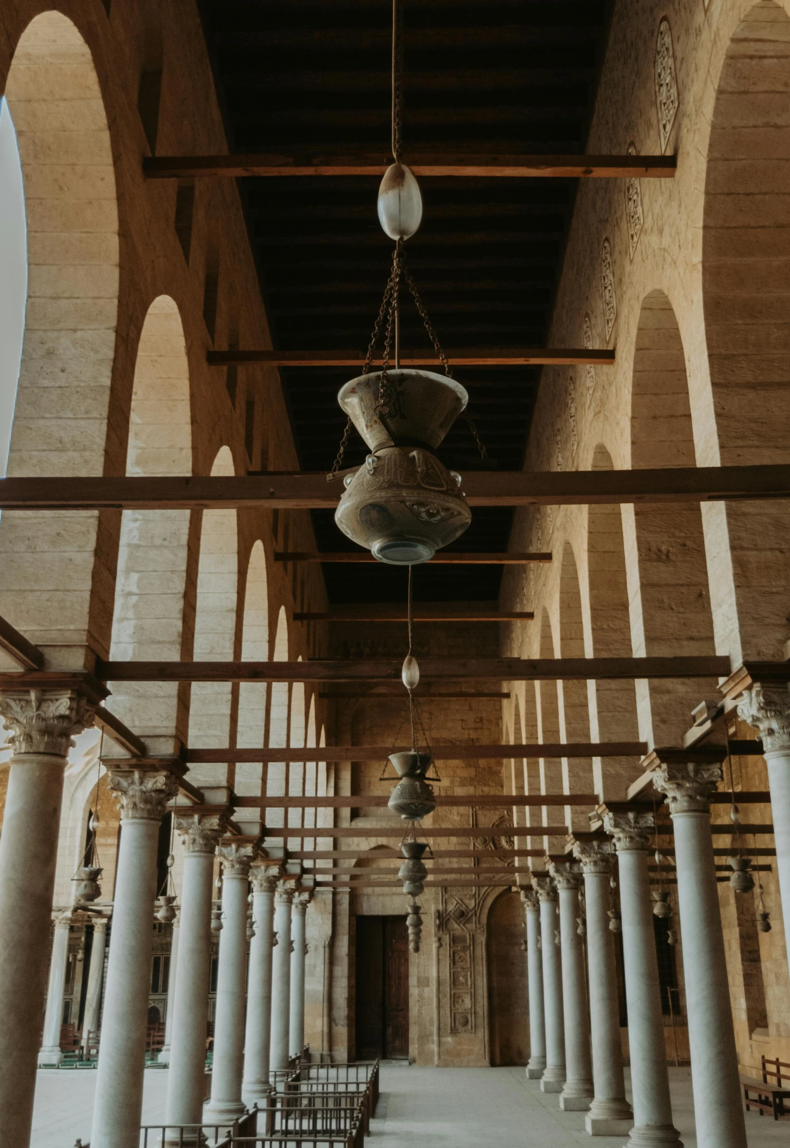 the inside of a building with columns and a chandelier, by Ahmed Yacoubi, unsplash contest winner, romanesque, in egypt, peaked wooden roofs, adjacent hallways, seen from outside