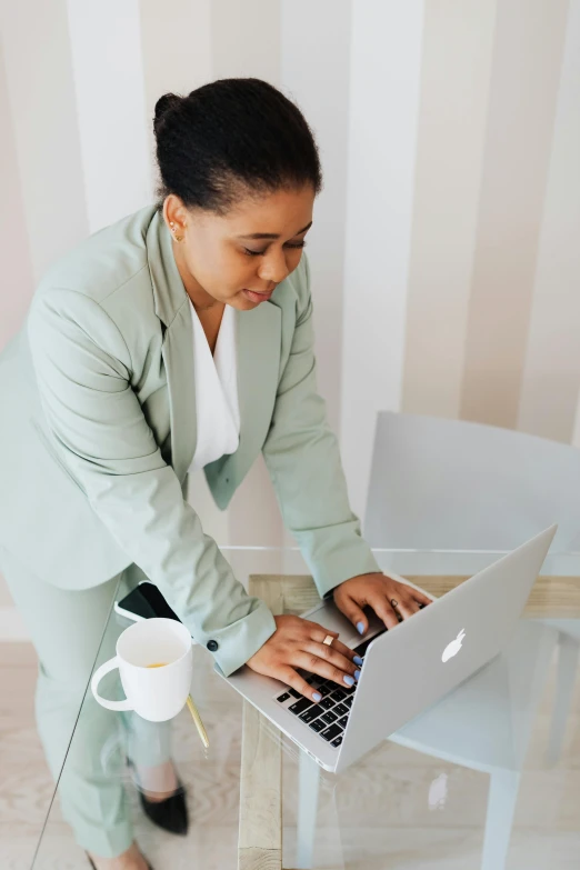 a woman sitting at a table using a laptop computer, pexels contest winner, standing elegantly, african american woman, wearing green suit, high angle