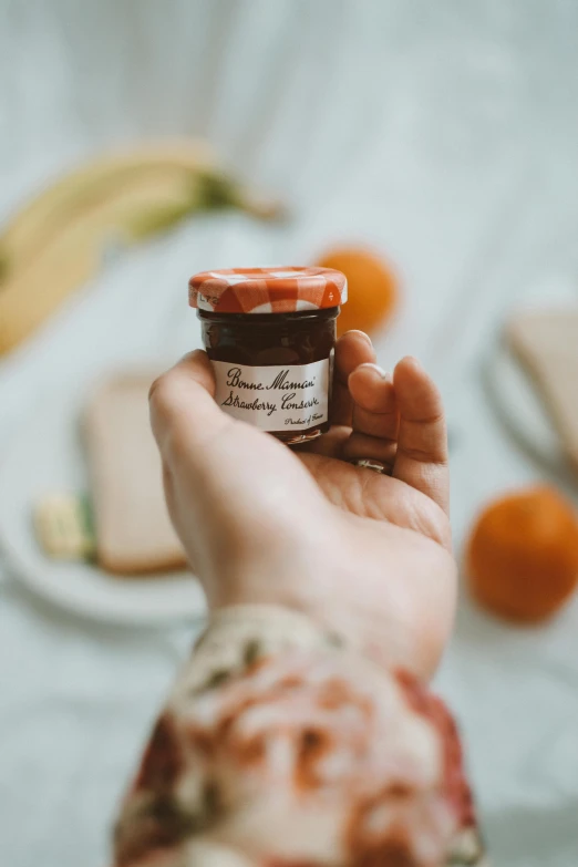 a person holding a jar of jam in their hand, product image, petite, thumbnail, brown