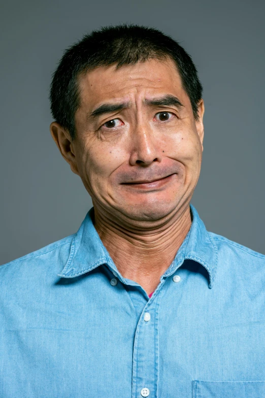 a man in a blue shirt posing for a picture, a picture, inspired by Kanō Naizen, confused facial expression, keng lye, on a gray background, sad eyebrows