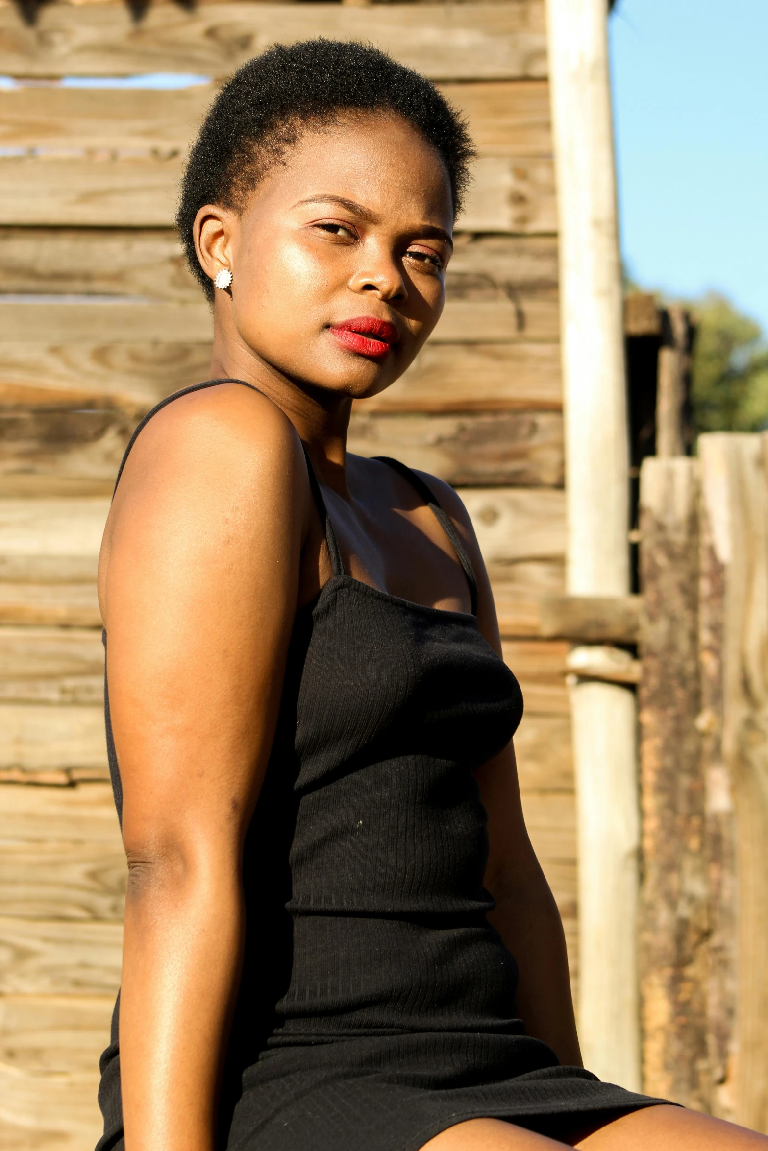 a woman sitting on top of a wooden bench, an album cover, inspired by Joze Ciuha, unsplash, she is wearing a black dress, standing in township street, 15081959 21121991 01012000 4k, headshot and bodyshot