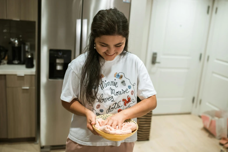 a woman standing in a kitchen holding a bowl of food, isabela moner, printed on a cream linen t-shirt, profile image, happy kid